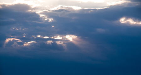 Ciemnoniebieskie niebo, promienie słoneczne przedzierają się przez chmury.