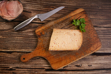 Raclette cheese with chilli pepper on a wooden cutting board