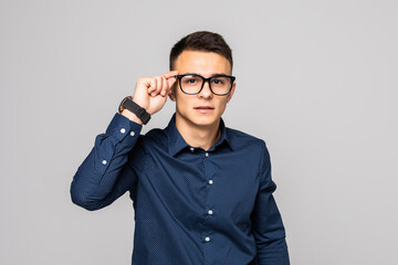 Optimistic portrait of a handsome young businessman in glasses standing against gray background