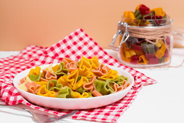 Ready-made Italian pasta with hearts in a white plate on a checkered white-red tablecloth. Valentine's day dinner.