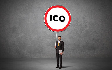 Young business person holdig traffic sign with ICO abbreviation, technology solution concept