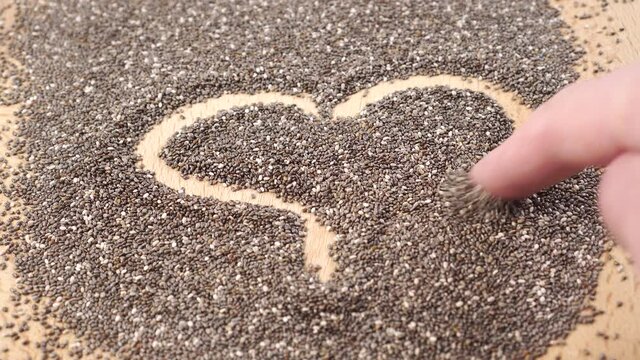 A man draws a heart shape with his finger on a heap of chia seeds close up. The concept of favorite dietary products and meals