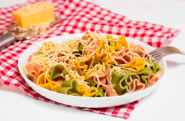 Ready-made Italian pasta with hearts in a white plate on a checkered white-red tablecloth and sprinkled with grated cheese. Valentine's day dinner.