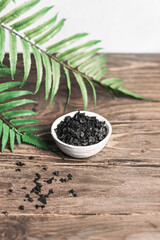 Spa - composition with Black Sea salt for body scrubbing on a wooden table. Green leaves in the background, blur, copy space.