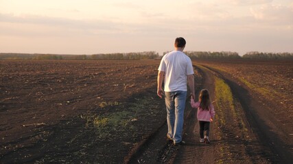 Happy child and father farmer are walking in field with crops. Little daughter holds daddy's hand....