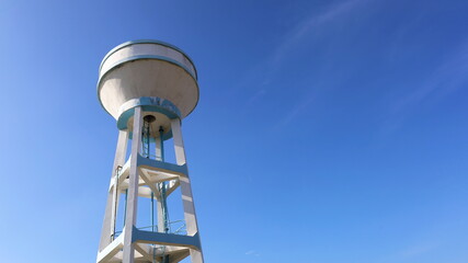 Concrete water tank on a tall tower. Large white storage tank for water supply systems in communities or workplaces. On a bright blue sky background with copy space. In view below. Selective focus