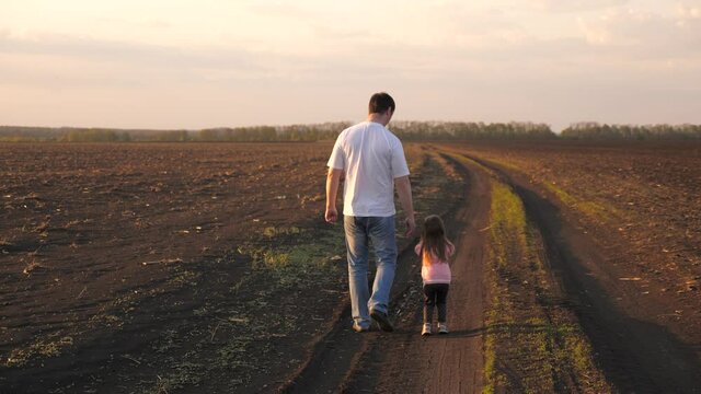 Happy child and father farmer are walking in field with crops. Little daughter holds daddy's hand. Kid and dad are traveling across field. child and dad walk on their own land. happy family, childhood