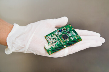 Womans hand with plastic gloves holding a computer circuit board on a grey background