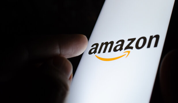 Amazon logo on a smartphone screen in a dark room and a finger pointing at it.