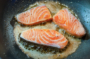 Slices of fresh salmon steak roasting with olive oil on a frying pan.