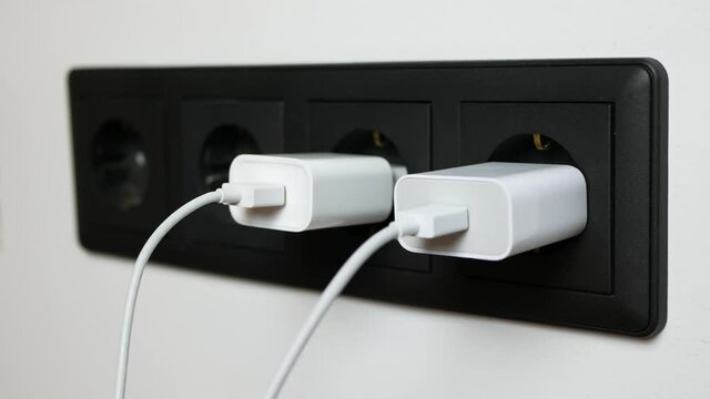 Man's hand pulling out the plugs from the sockets after powering the electronic devices, Four black power sockets on white wall 