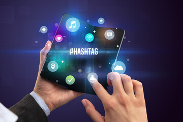 Businessman holding a foldable smartphone with #HASHTAG inscription, social media concept