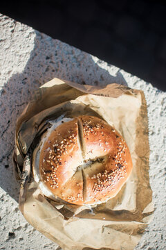 Everything Bagel Sandwich Cut In Half On Brown Paper In The Sun.