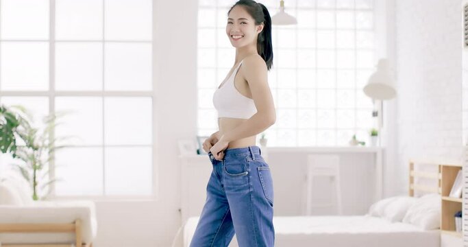 Young slim woman in  big jeans showing her diet results at home
