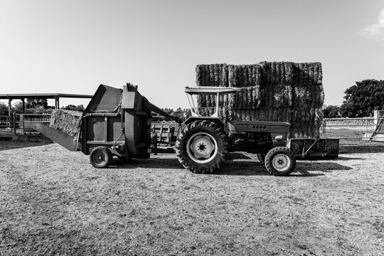 A grayscale shot of a tractor and hay blocks at a farm