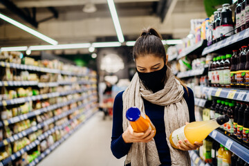 Young woman wearing protective face mask shopping in a supermarket,buying bio food and natural juice.Eating healthy food during coronavirus COVID - 19 pandemic.Vitamins and immune system.Grocery shop