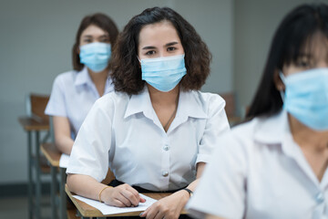 Cheerful college students in the classroom wear protective face masks and use antiseptic for coronavirus prevention during coronavirus pandemic. Group of students wearing protection masks in class.