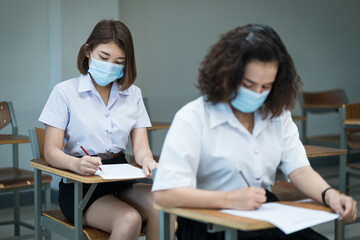 Cheerful college students in the classroom wear protective face masks and use antiseptic for coronavirus prevention during coronavirus pandemic. Group of students wearing protection masks in class.