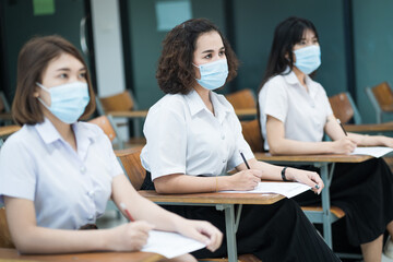 Fototapeta premium Cheerful college students in classroom wear protective face masks and use antiseptic for coronavirus prevention during coronavirus pandemic. Group of students wearing protection masks in class.