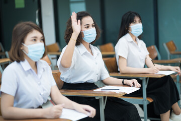 Cheerful college students in classroom wear protective face masks and use antiseptic for coronavirus prevention during coronavirus pandemic. Group of students wearing protection masks in class.