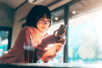 Young adult asian woman using mobile phone for social media background with window and warm...
