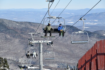 Fototapeta premium Chairlift with people at Stowe Ski Resort in Vermont, view to the Mansfield mountain slopes, December fresh snow on trees early season in VT, hi-resolution image