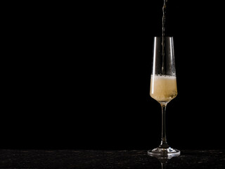 A stream of sparkling wine flowing into a tall glass on a black background.