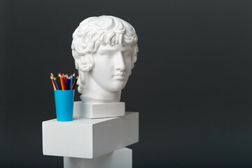 Antinous ' plaster head stands next to a set of pencils in a glass. Concept of drawing and creative activities