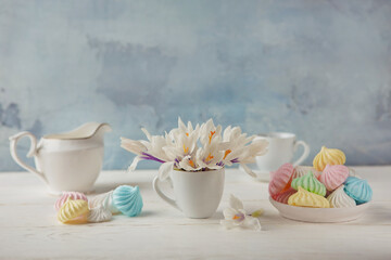 Romantic Breakfast with a Cup of tea, Crocus flowers and sweet multi-colored meringue on the wooden table.