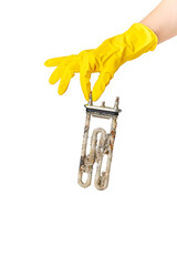 A hand in a yellow glove holds the heating element of a washing machine or dishwasher, covered with a lime coating. The concept of replacement, repair or disposal.