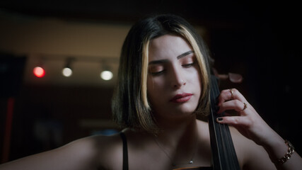 Young beautiful woman with short hair in black dress plays the cello in a modern venue. Close-up