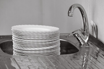 A big pile of dishes in the sink under the water tap