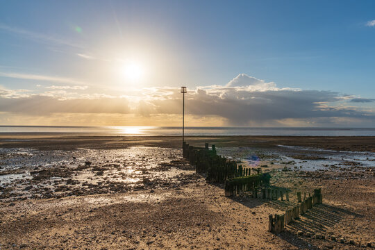 Groynes and the setting sun at the North Beach in Heacham, Norfolk, England, UK