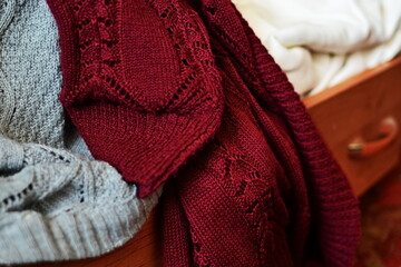 Knitted homemade clothes with different color and pattern lie on open dresser