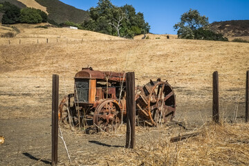Vintage rusty tractor in open field of hay in fence portion