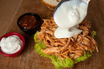Putting yogurt sauce on shredded chicken sandwich