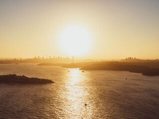 Fototapeta premium Panoramic sunset aerial drone view of famous Sydney Harbour with the CBD city centre skyline in the background. South Head, a headland to the north of Watsons Bay suburb, in the foreground.