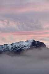 Montaña nevada, puesta de sol, cima de la montaña entre mar de nubes.