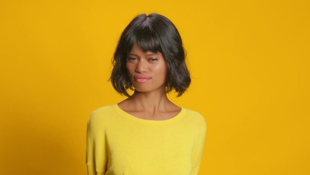 Displeased dark skinned woman looks with aversion and dissatisfaction aside dislikes something says its not good dressed in casual jumper isolated over yellow background. Negative emotions concept