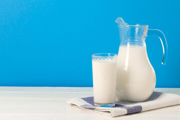 Glass and pitcher of milk against blue background