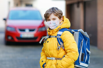 Little kid boy wearing medical mask on the way to school. Child backpack satchel. Schoolkid on cold autumn or winter day with warm clothes. Lockdown and quarantine time during corona pandemic disease
