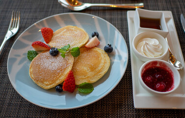 A top view of a dessert table with sweet pancakes, dipping sauces, and fruits on a plate