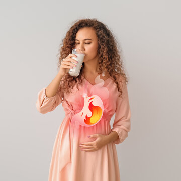 Pregnant African-American woman drinking milk to relieve heartburn on grey background