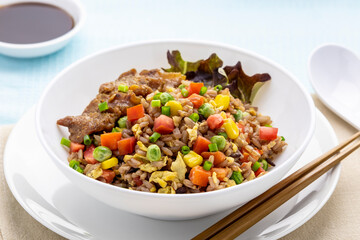 Fried brown rice with colorful vegetables, topped with fried pork
