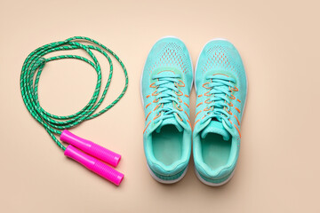 Sportive shoes and jumping rope on color background