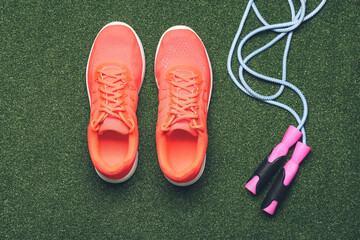 Sportive shoes and jumping rope on color background