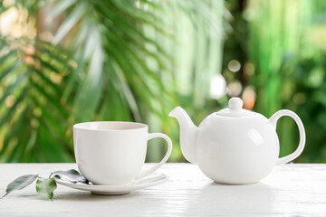 Cup of green tea and teapot on table against blurred  background