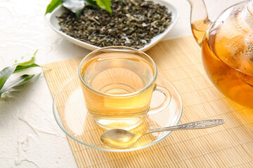 Cup of green tea, teapot and dry leaves on bamboo mat
