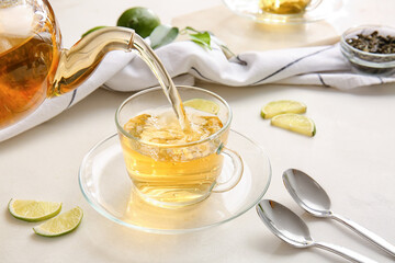 Pouring green tea from teapot into cup on table