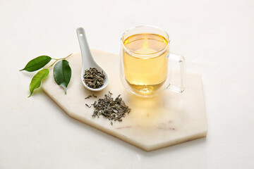 Cup of green tea and spoon with dry leaves on white background